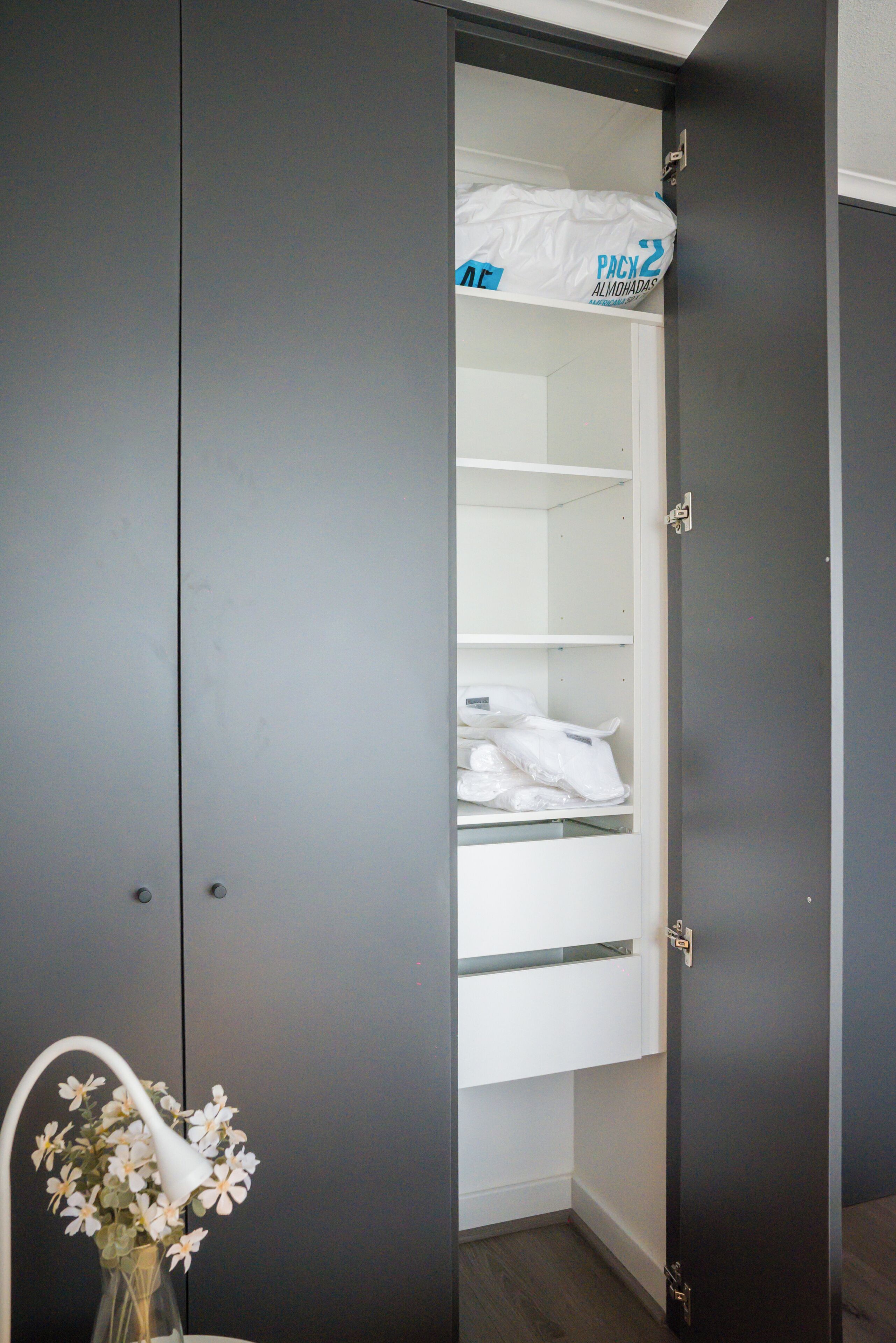 Een kast met open deuren, waar netjes opgevouwen kleding en een witte tas met de tekst 'PACK 2' in zichtbaar is.