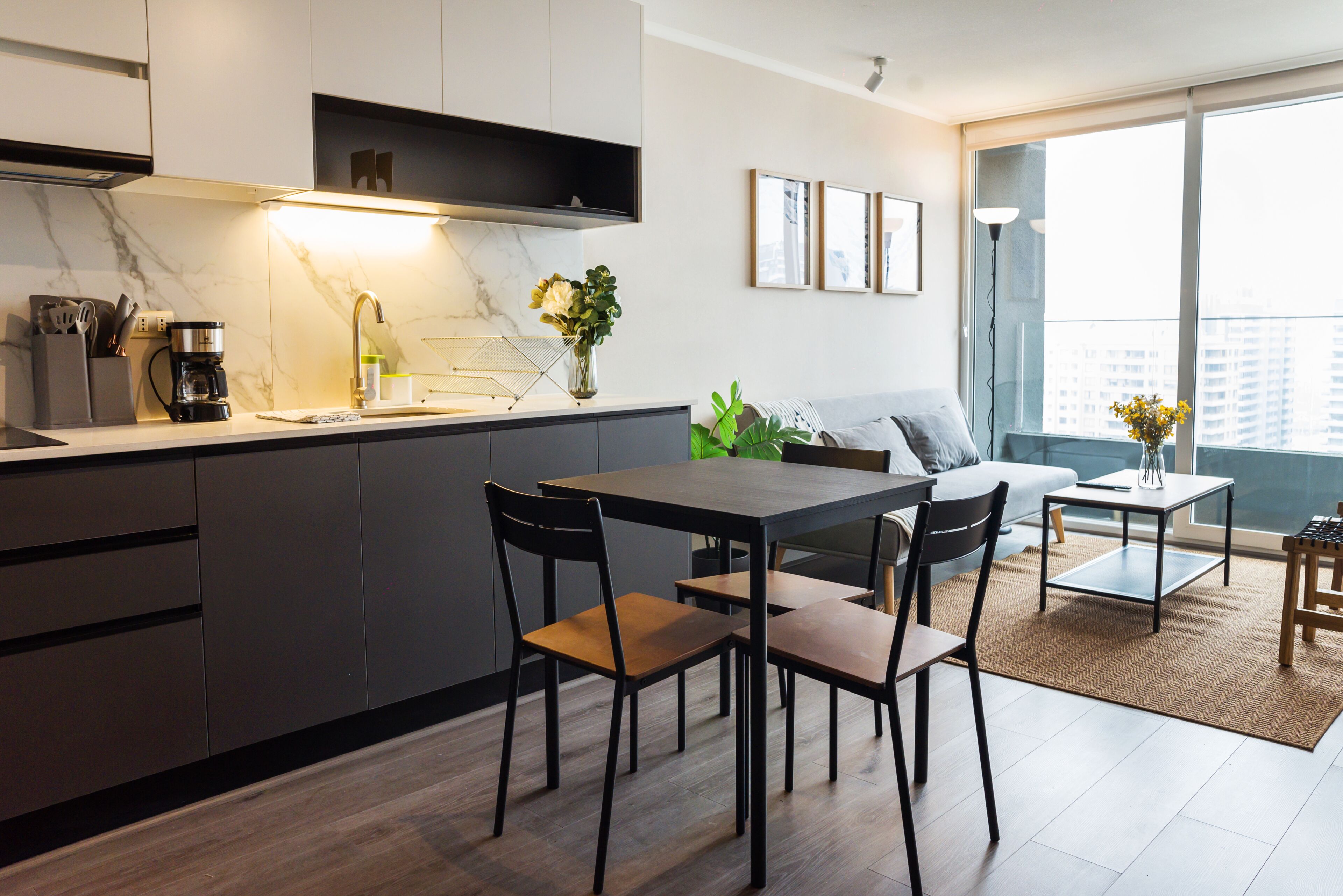 Una cocina moderna con comedor, una cafetera y vistas a la ciudad a través de amplios ventanales.