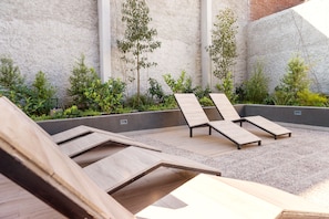A rooftop terrace with wooden loungers, a concrete wall, and various plants. - Seminario Apartments by Andes STR (Ñuñoa)