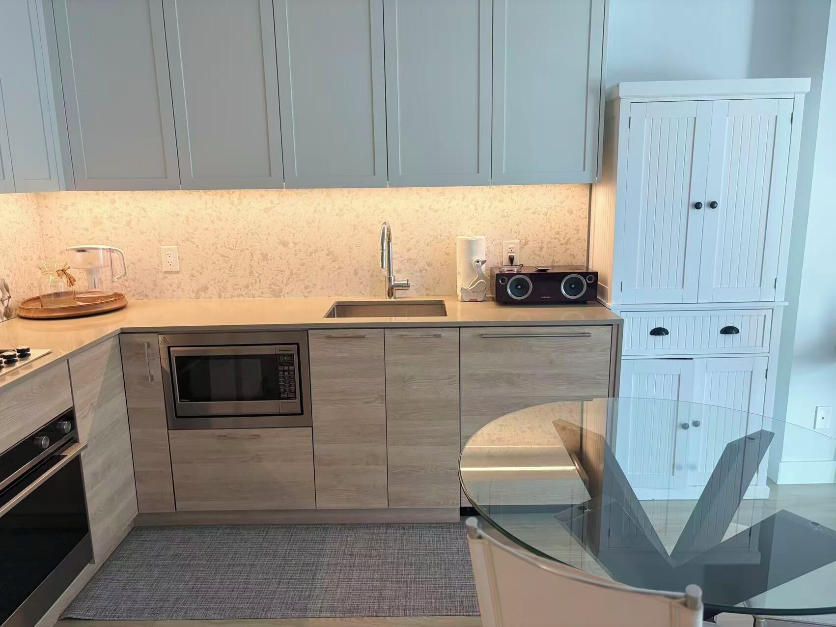 A modern kitchen with a built-in microwave, a sink, and a glass-top dining table.