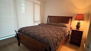 Un dormitorio con cama, mesita de noche, lámpara y ventana.