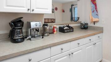 A kitchen with white cabinets, a coffee maker, a kettle, a coffee grinder, and a coffee bean container.