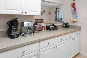A kitchen with white cabinets, a coffee maker, a kettle, a coffee grinder, and a coffee bean container. - Spacious 4BR | Near UF & Shands | Pool + Gym (Gainesville)