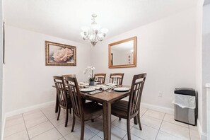 Ein Esszimmer mit Holztisch, sechs Stühlen, einer Chandelierleuchtre, einem gerahmten Gemälde und einem Spiegel an der Wand.