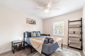 A bedroom with a bed, a nightstand, a window, a ceiling fan, and a storage unit. - Spacious 4BR | Near UF & Shands | Pool + Gym (Gainesville)