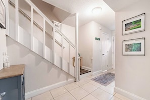 A hallway with a staircase, a door labeled 'FLORIDA,' and a small table with a bottle. - Spacious 4BR | Near UF & Shands | Pool + Gym (Gainesville)