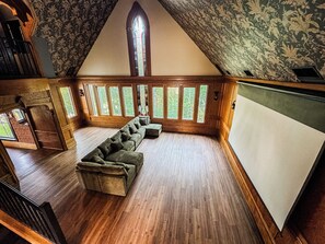 A room with a sloped ceiling, a large window with multiple panes, a wooden bench, and a whiteboard.