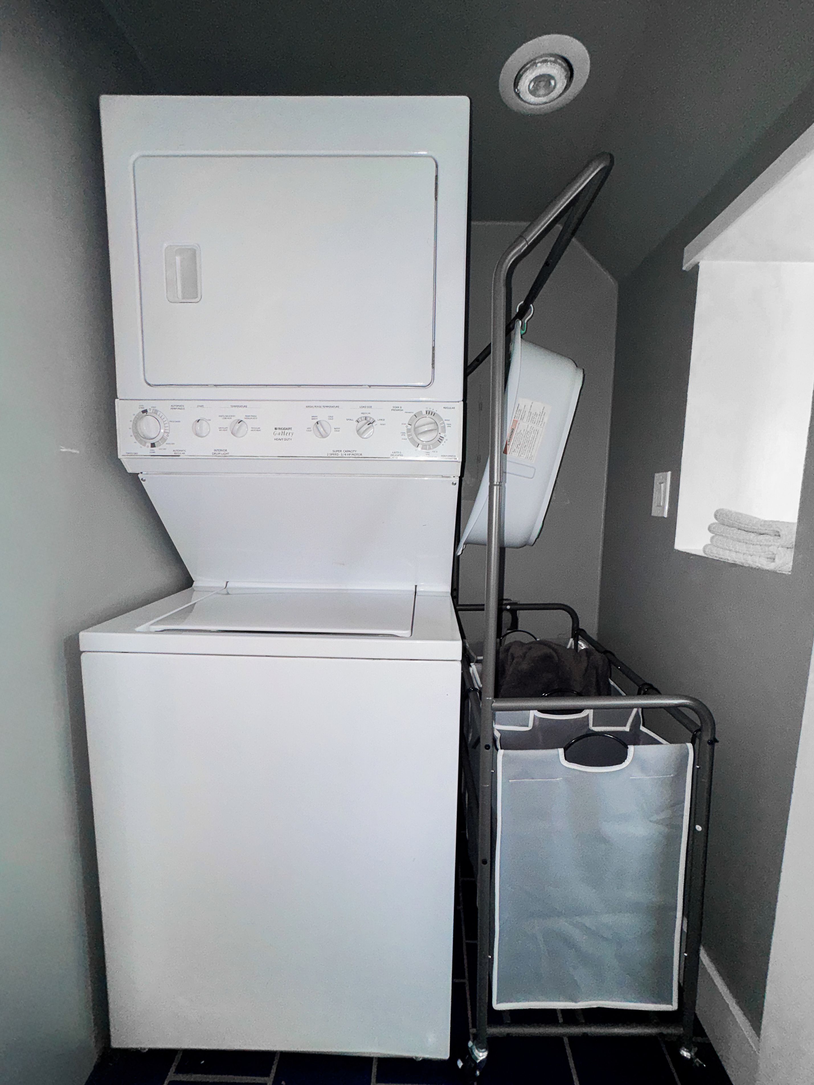 Un espace buanderie compact comprenant une laveuse et une sécheuse superposées, un étendoir métallique et un petit bac de rangement.