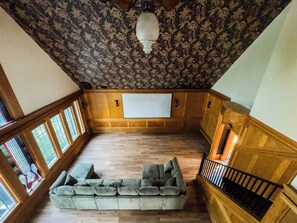 A room with a wooden ceiling, a large window, a sofa, and a staircase.