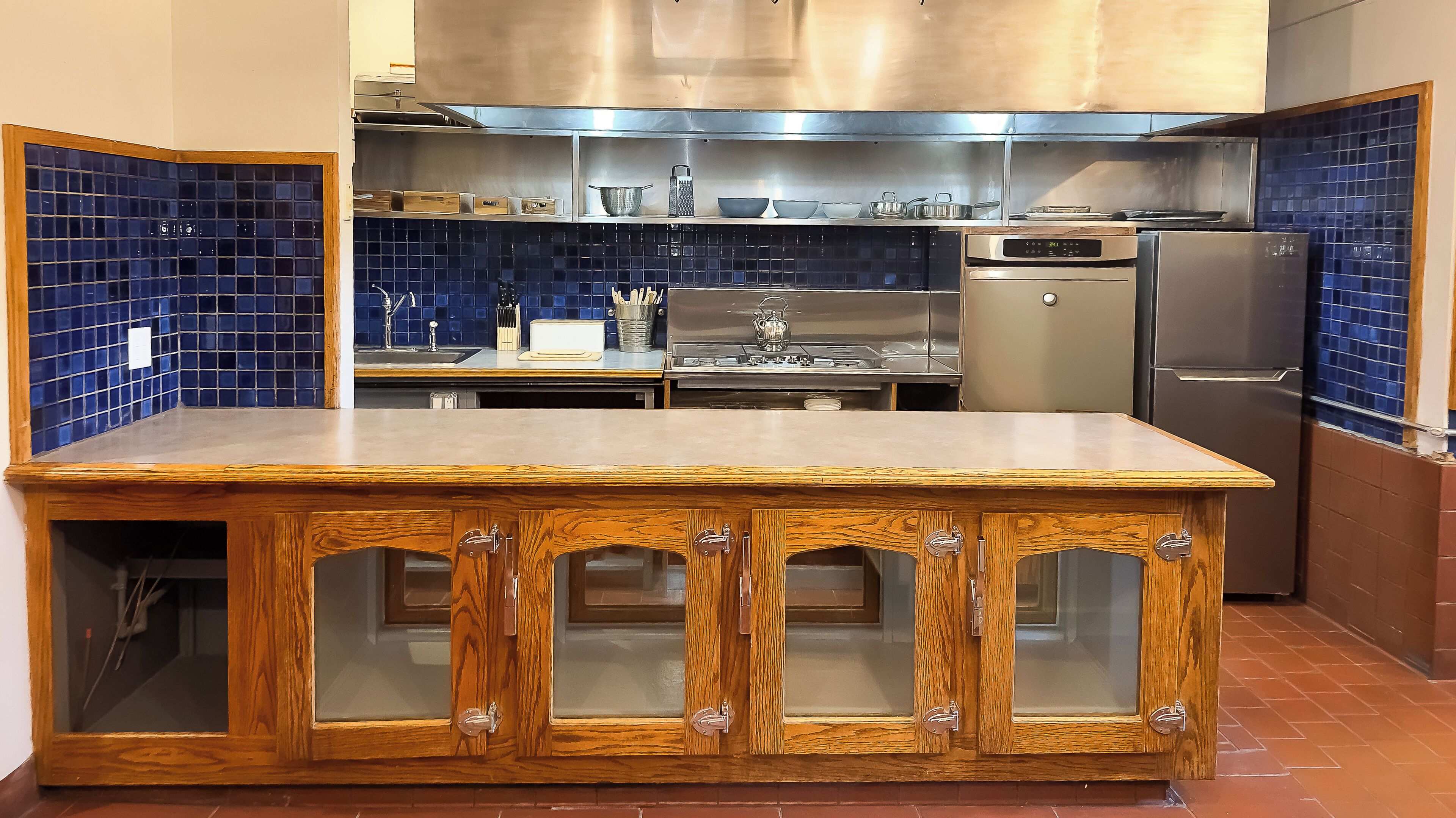 Une cuisine dotée d’un îlot central en bois, d’appareils électroménagers en acier inoxydable et d’un dosseret de crédence recouvert de carreaux bleus.