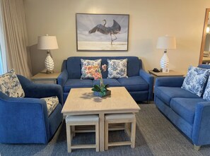 A hotel room with a blue sofa set, a small wooden coffee table, and a framed picture of a bird on the wall. - 2-bedroom apt BEACHFRONT on Marco Island - Eagle's Nest Resort PRESIDENT'S WEEK! (Marco Island)