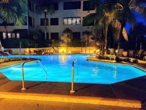 A swimming pool with a metal railing, surrounded by palm trees and a building with multiple windows. - 2-bedroom apt BEACHFRONT on Marco Island - Eagle's Nest Resort PRESIDENT'S WEEK! (Marco Island)
