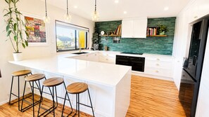 A modern kitchen with a large island, bar stools, a view of the outside, and a green backsplash.