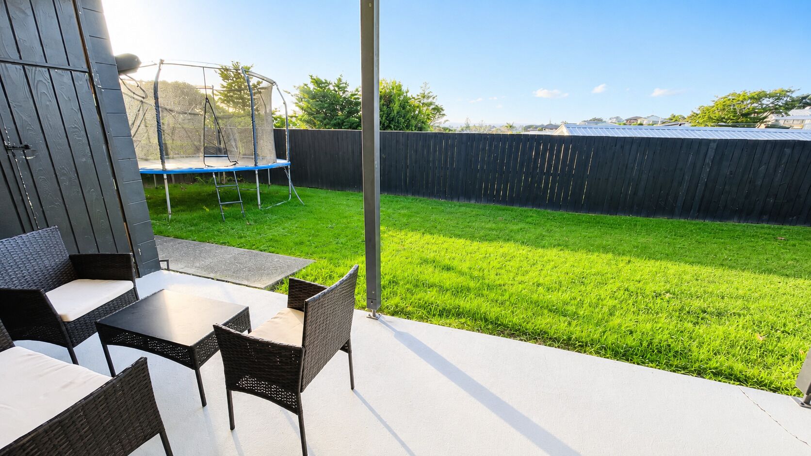 An outdoor patio with a table and chairs, a trampoline, and a well-maintained lawn.