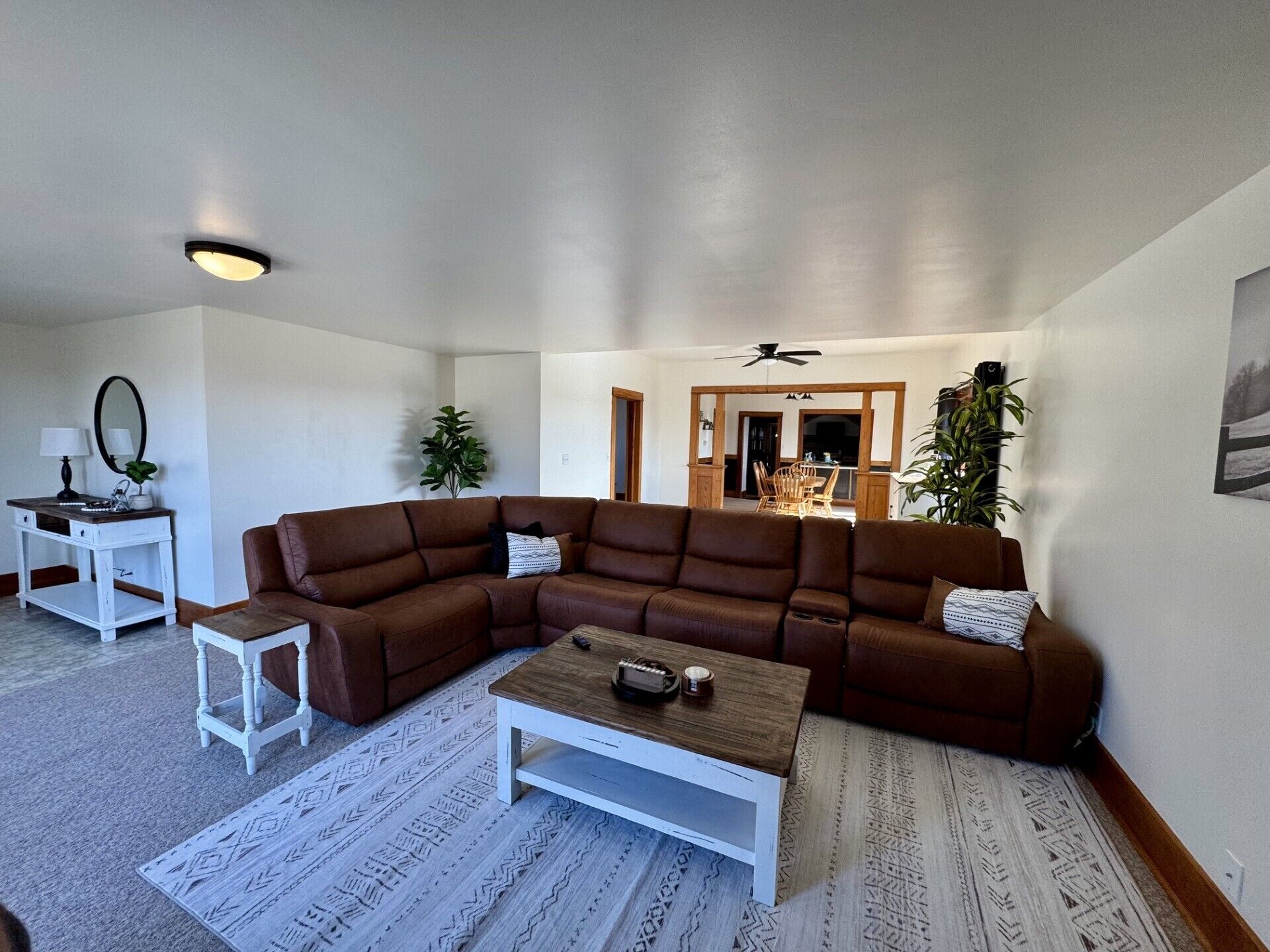 Ein Wohnzimmer mit einem braunen Ecksofa, einem weißen Couchtisch, einem kleinen weißen Beistelltisch und einem gemusterten Teppich.
