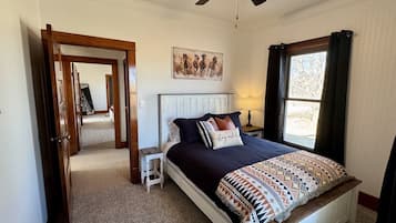 A bedroom with a bed, a ceiling fan, a window, and a door leading to another room.