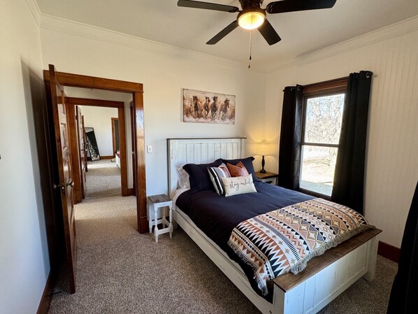 Un dormitorio con cama, ventilador de techo, ventana y puerta que da a otra habitación.