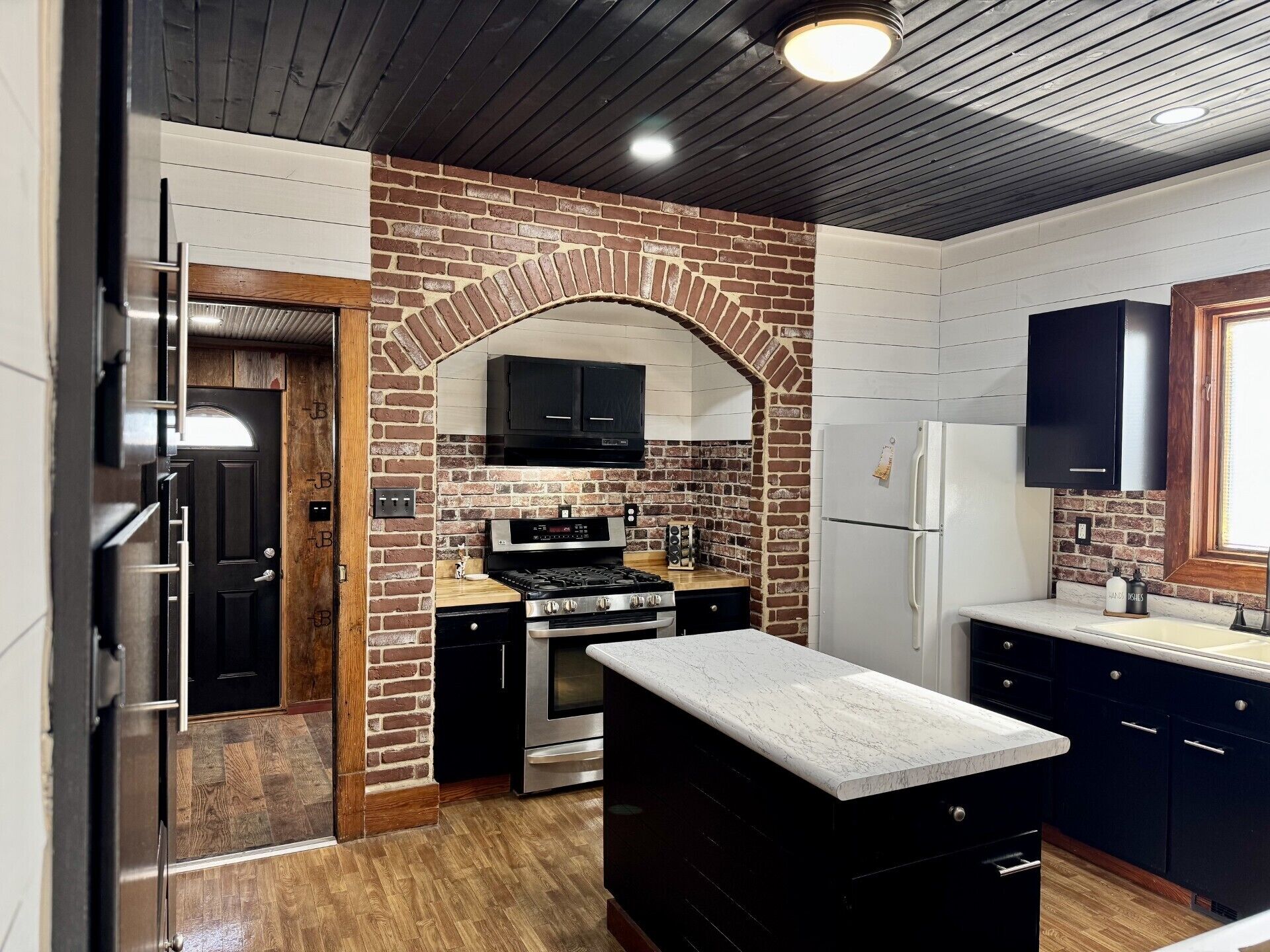 A kitchen with a brick archway, stainless steel appliances, and a marble countertop.
