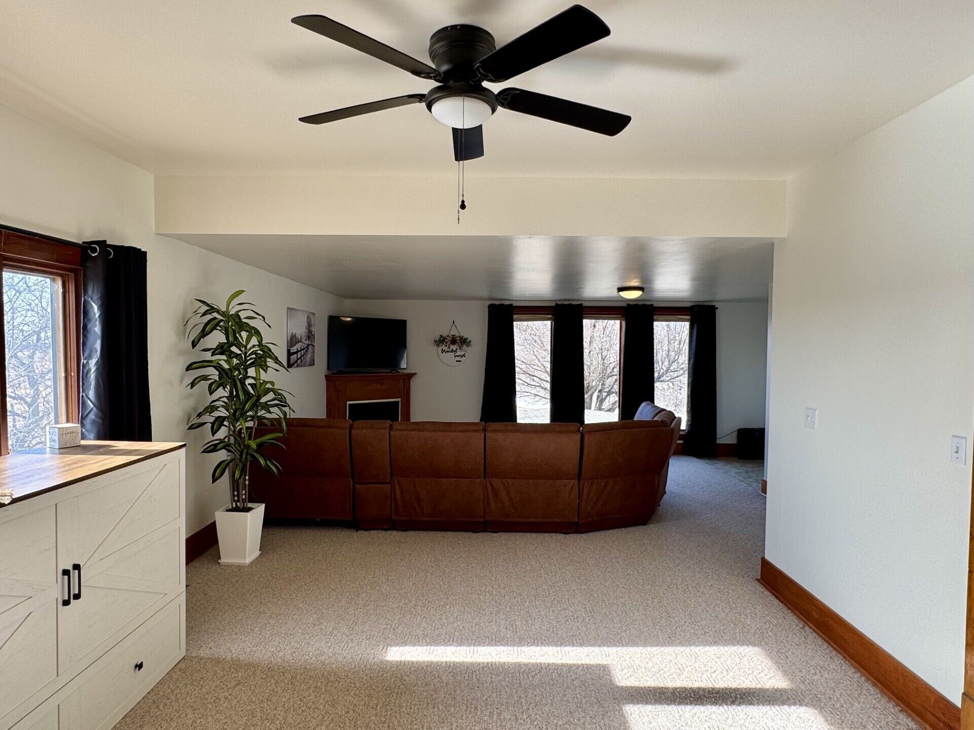 A spacious living area with a ceiling fan, a large window, a sofa, and a potted plant.