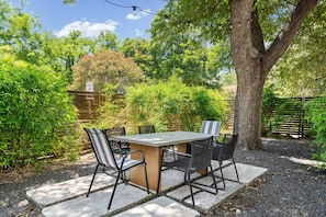 Eine Terrasse im Freien mit Tisch und Stühlen, umgeben von Bäumen und einem Holzzaun.