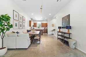 A modern kitchen with wooden cabinets, a dining area with a table and chairs, and a living room with a sofa and a plant. - 3 Levels of Living 2 Lounges, 2 K Suites + Pool Table E ATX Outdoor Living (Austin)