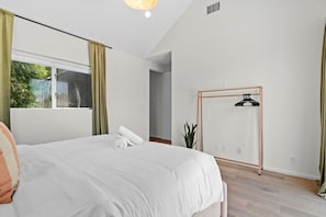 A bedroom with a bed, a hanging clothes rack, a potted plant, and a window with curtains. - 3 Levels of Living 2 Lounges, 2 K Suites + Pool Table E ATX Outdoor Living (Austin)