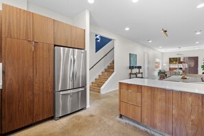 Eine moderne Küche mit Holzschränken, einem Edelstahlkühlschrank, einer weißen Arbeitsplatte und einer Treppe, die ein weiteres Geschoss hinaufführt.
