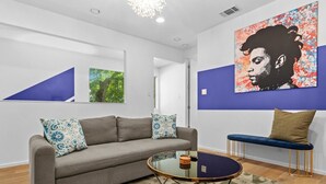A modern living room with a grey sofa, blue patterned pillows, a round glass coffee table, and a blue bench with a cushion. - 3 Levels of Living 2 Lounges, 2 K Suites + Pool Table E ATX Outdoor Living (Austin)