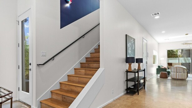 A modern interior with a wooden staircase, a console table with lamps, and a view through a glass door. - 3 Levels of Living 2 Lounges, 2 K Suites + Pool Table E ATX Outdoor Living (Austin)