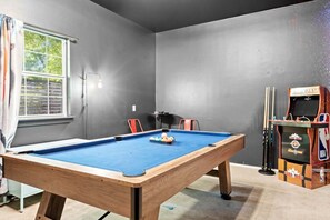 A pool table with balls, a pool cue rack, and a basketball arcade machine in a room with grey walls. - 3 Levels of Living 2 Lounges, 2 K Suites + Pool Table E ATX Outdoor Living (Austin)