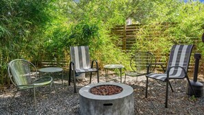 An outdoor seating area with chairs and a table, surrounded by dense foliage and a wooden fence. - 3 Levels of Living 2 Lounges, 2 K Suites + Pool Table E ATX Outdoor Living (Austin)