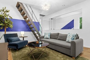 A modern living room with a sofa, armchair, coffee table, and a staircase. - 3 Levels of Living 2 Lounges, 2 K Suites + Pool Table E ATX Outdoor Living (Austin)