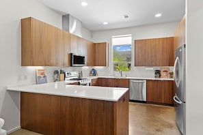 A modern kitchen with wooden cabinets, a central island, stainless steel appliances, and a window providing a view of the outdoors. - 3 Levels of Living 2 Lounges, 2 K Suites + Pool Table E ATX Outdoor Living (Austin)