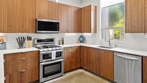 A modern kitchen with wooden cabinets, stainless steel appliances, and a window providing natural light. - 3 Levels of Living 2 Lounges, 2 K Suites + Pool Table E ATX Outdoor Living (Austin)