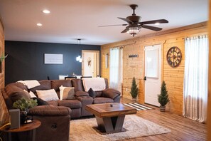 A cozy living room with a brown leather sofa, a wooden coffee table, and a ceiling fan. - 3BR/2BA • 4-6 Min to Huzzah Valley & Bass River Resort (Steelville)