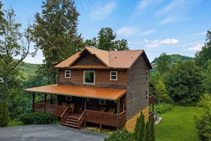 A two-story log cabin with a porch and a covered deck, surrounded by lush greenery and hills. - Peaceful Wooded Retreat - Arcade, Hot Tub + Fire Pit (Sevierville)