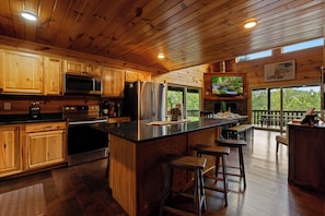 A modern kitchen with wooden cabinets, stainless steel appliances, and a large island with bar stools. - Peaceful Wooded Retreat - Arcade, Hot Tub + Fire Pit (Sevierville)