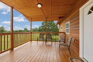 Eine Holzterrasse mit Geländer, zwei Stühlen, einer Verandaleuchte und Blick auf eine grüne Landschaft.