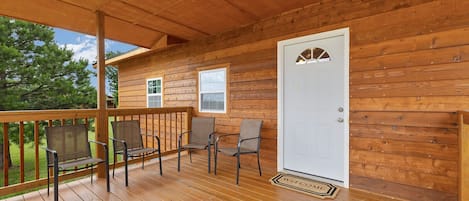 Eine Holzhütte mit Veranda, einer weißen Tür und drei Stühlen.