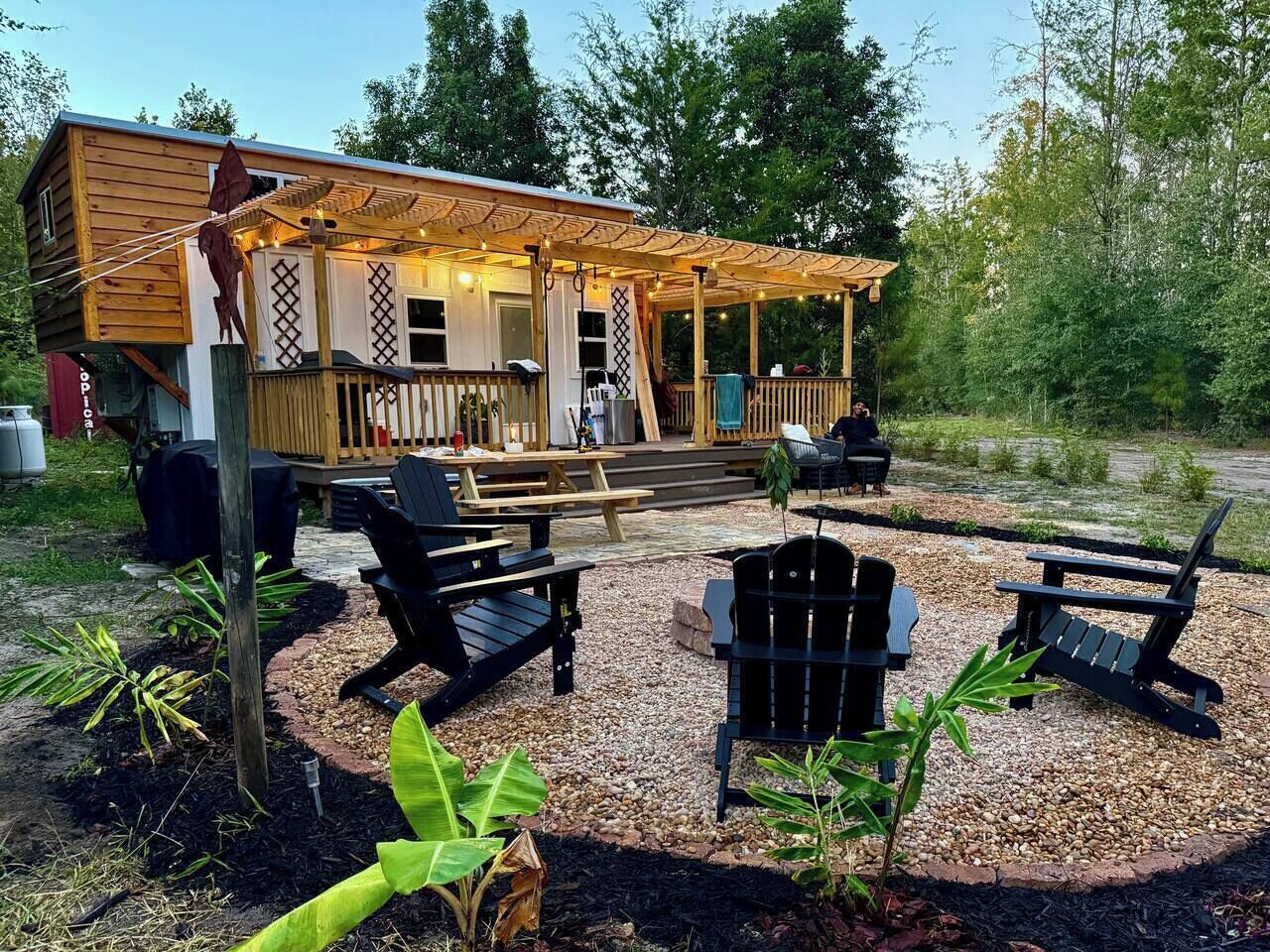 A wooden deck with outdoor seating, including chairs and a table, surrounded by gravel and plants.