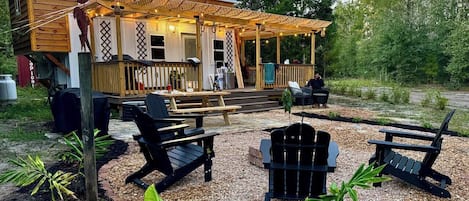 A wooden deck with outdoor seating, including chairs and a table, surrounded by gravel and plants.