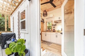 Una terraza de madera con una parrilla, una planta en maceta y una ventana con persianas.