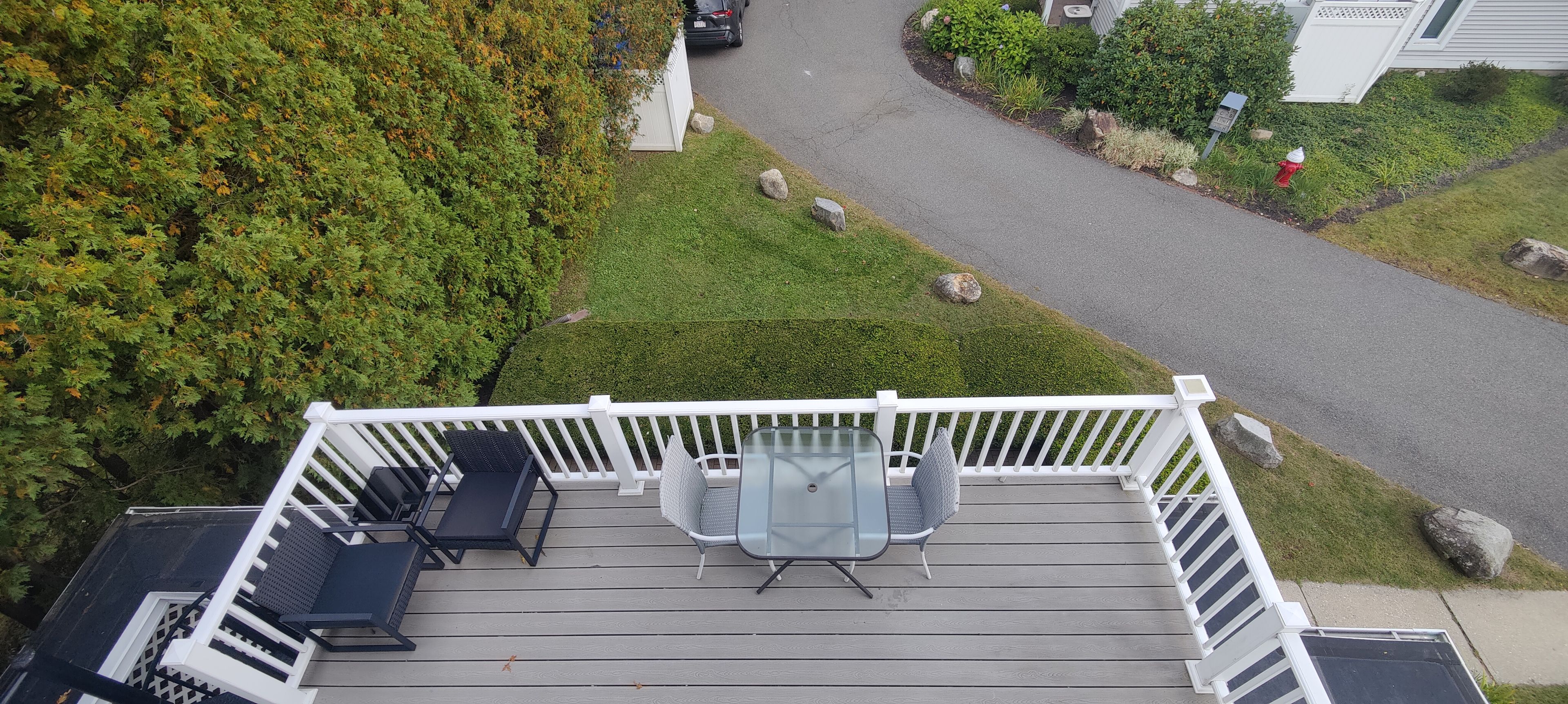 A deck with outdoor furniture, a glass table, and a white railing.
