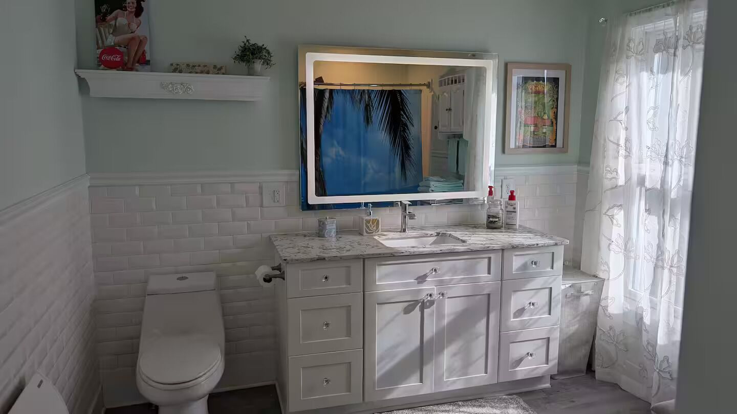 Une salle de bain avec des toilettes blanches, un lavabo doté d’un plan de travail en marbre et un miroir au-dessus du lavabo.