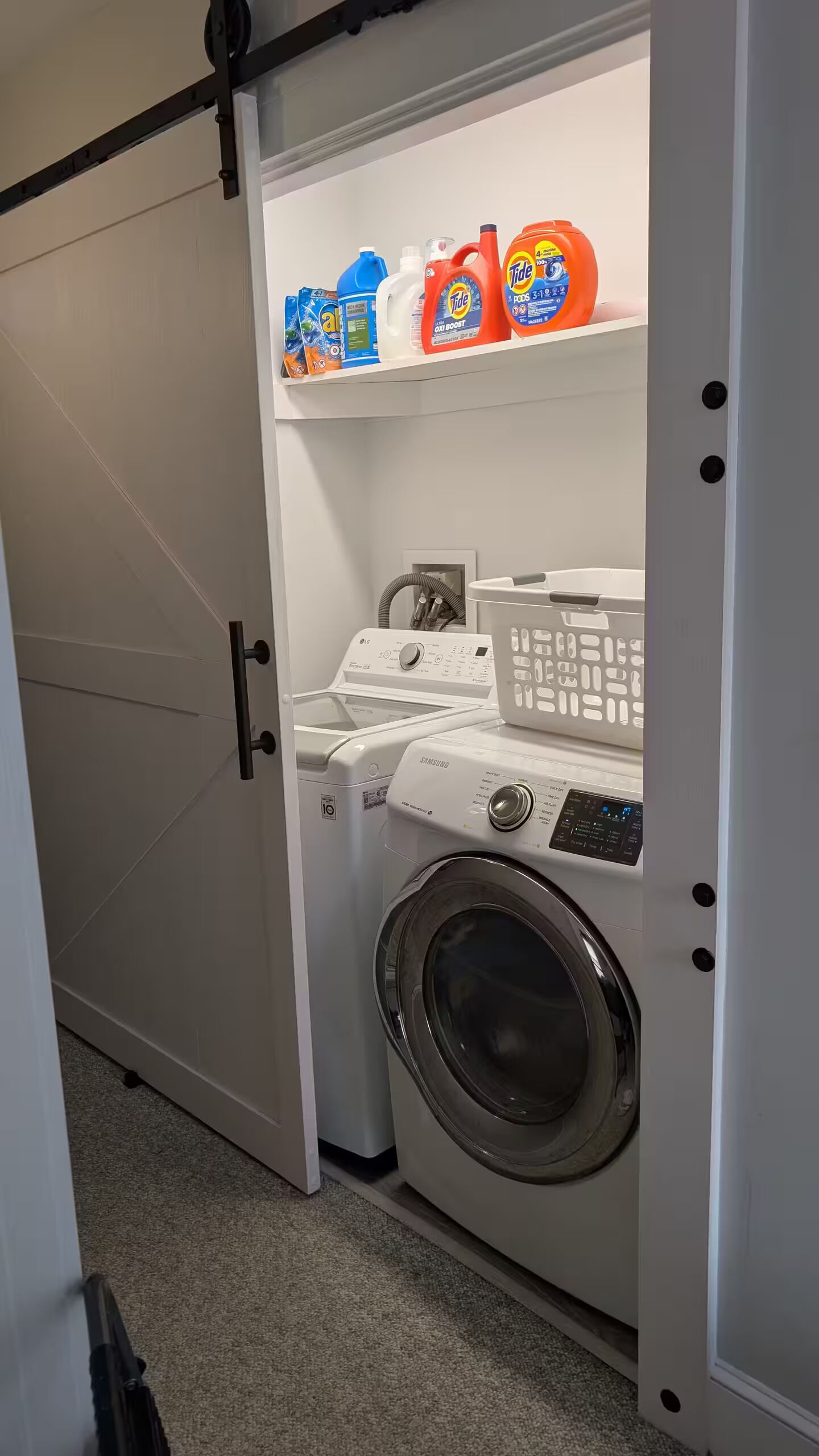 Ein kleiner Hauswirtschaftsraum mit einer Waschmaschine mit Frontlader, einem Trockner und einem Regal mit verschiedenen Waschmitteln.