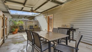 Un patio exterior con una mesa, sillas, ventilador de techo y una parrilla.