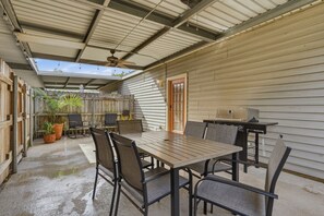 Eine Terrassenanlage mit Tisch, Stühlen, einem Deckenventilator und einem Grill.