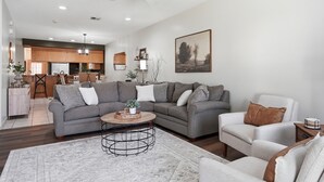 Un salón con un sofá seccional gris, un sillón blanco y una mesa de centro.