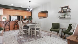 Una cocina moderna con armarios de madera, un comedor con mesa y sillas, y un espacio de sala con un sillón verde y una mesita auxiliar.