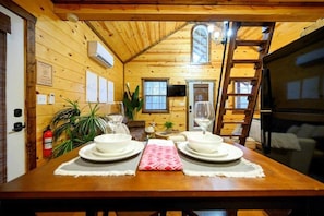 A wooden cabin interior with a dining table set for two, a fire extinguisher, and a ladder. - Beaver's Little Lodge I Couples Cabin I Romantic (Hochatown)